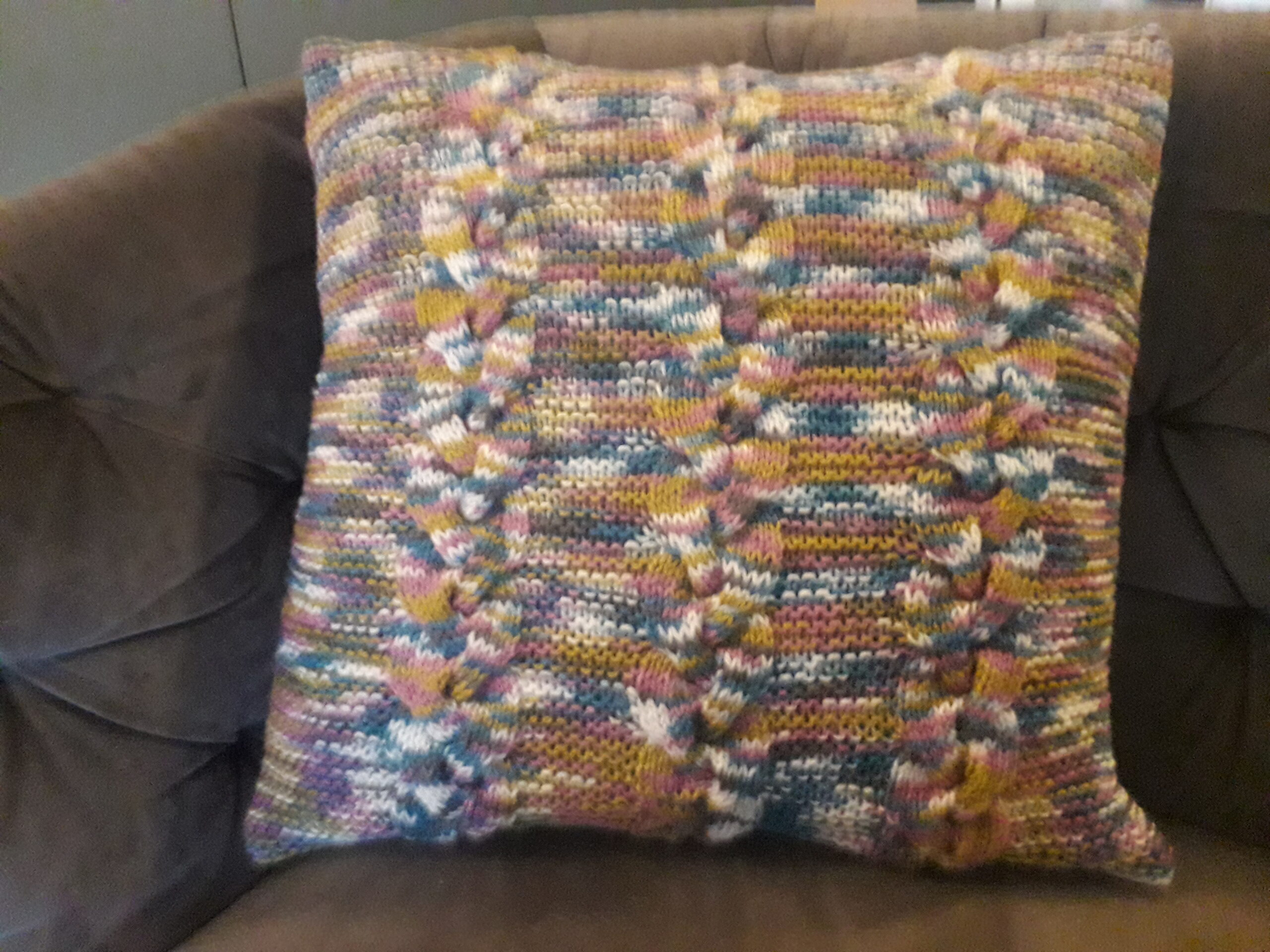 sfeerfoto van handgebreid kussen op een grijze bank met kabels