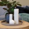 sfeerfoto met ivoren kaarsen op een blad op de tafel met een plant erachter