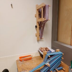 een foto van een bandgweefgetouw op de werktafel en eentje hangend aan de muur